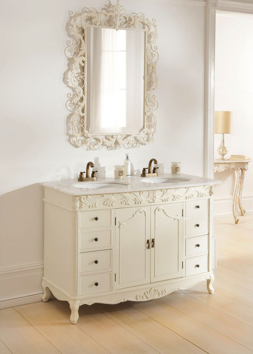 Łazienkowe meble stylizowane na antyki: francuska biała szafka, komoda z drzwiczkami, szufladami, marmurowym blatem na umywalki, bogato zdobione lustro łazienkowe i mały stolik.