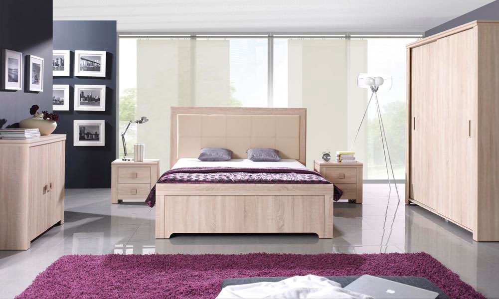Meble do sypialni kluczem do relaksu: drewniane łóżko, szafki nocne, duża szafa, komoda, szare poduszki, fioletowa pościel i dywan
